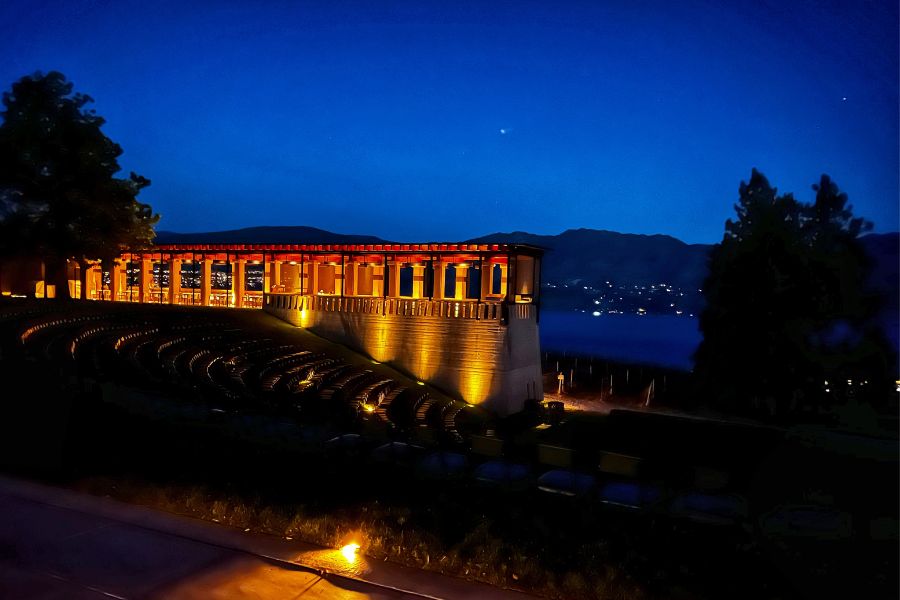 Nighttime photo of a terrace illuminated by lights overlooking a lake. 