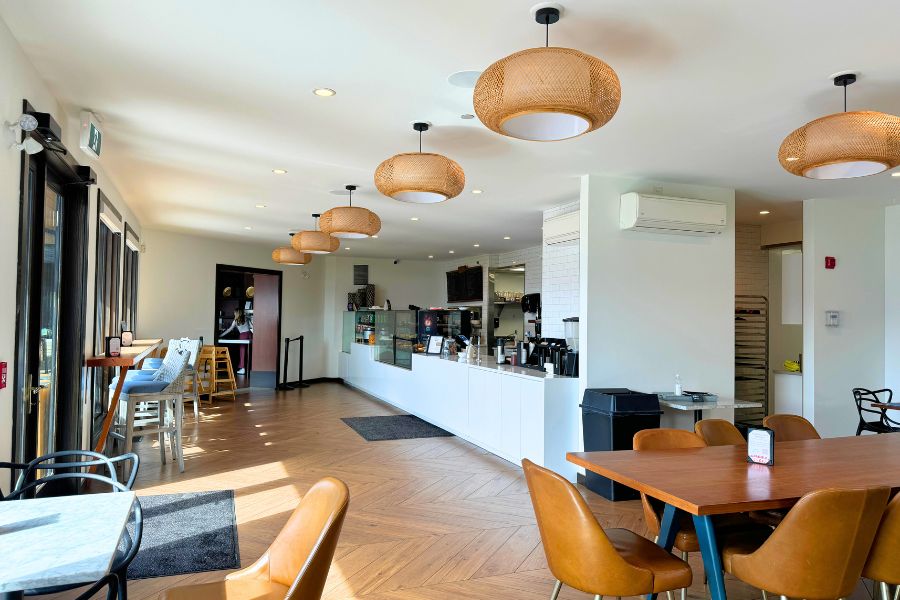 Picture of the inside of a cafe. Tan wicker lights line the celing, hard wood floors and warm wood tables. 