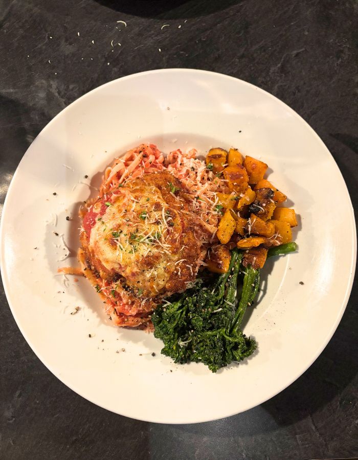 Chicken Parmesean on a white plate with broccolini on the side