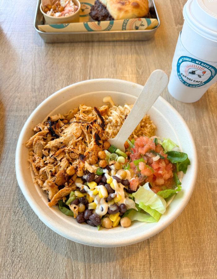 A bowl with rice, chicken, corn, beans, lettuce and tomato salsa on the side. 