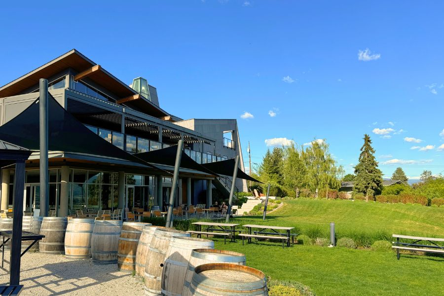 View looking back at the restaurant from the grass. A two lovel modern building surrounded by grass and picnic tables